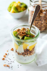 Yogurt granola parfait with mango,kiwi, tropical fruits аnd сhia seeds, layered dessert or breakfast. Selective focus.