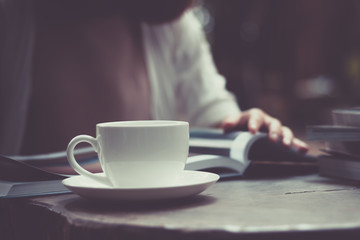 Woman is reading a book and drinking coffee in the garden.