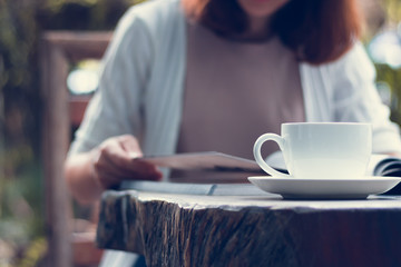 Woman is reading a book and drinking coffee in the garden.