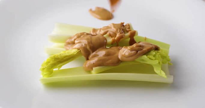 Celery stalks on a white plate with peanut butter messily covering the vegetables.