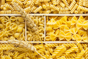 Several kinds of pasta in a wooden box. Two sprigs of wheat