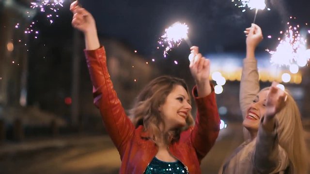 best girlfriends have fun together in night city, holding in their hands a sparkling fireworks in slow motion