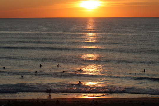 Surfers Waiting For A Wave Near The Beach At Sunset