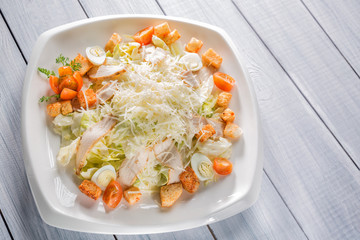 Healthy green organic caesar salad with cheese on white plate and wooden table