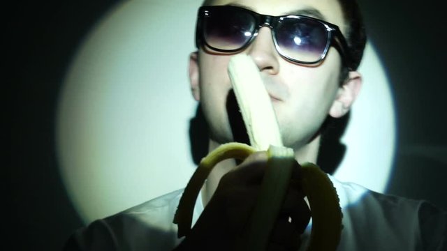 Man in sunglasses is eating banana in light beam