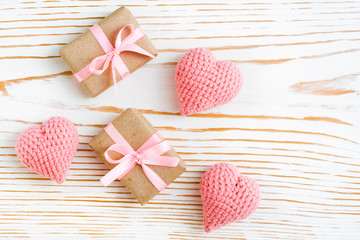 Пара упакованных подарков с розовой лентой и вязанные сердца на белом деревянном фоне - obrazy, fototapety, plakaty