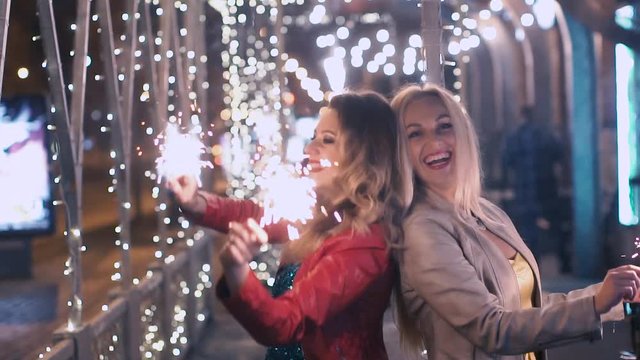 Beautiful girls with sparkling fireworks celebrate a holiday in the night city and have fun. SLOW MOTION