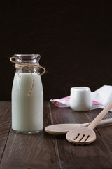 Milk in a glass bottle and kitchen tools on a wooden background.