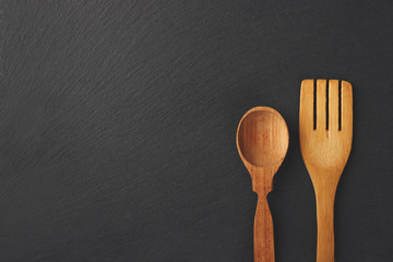 Wooden spoon and fork on the black stone background