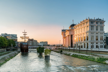 Wide view of the center of skopje Macedonia with the river Vardar, ship and surrounding buildings, late afternoon with sunset. - obrazy, fototapety, plakaty