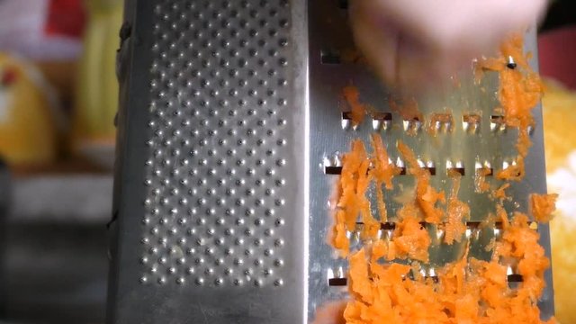 Female rubs carrots at a grater on a chopping board. Carrots on a grater rubbed on the kitchen. Cutting Carrot Grater