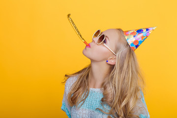 portrait of funny blond woman in birthday hat and blue shirt on yellow background. Celebration and party.
