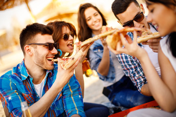 Happy people eating pizza and have fun on the beach