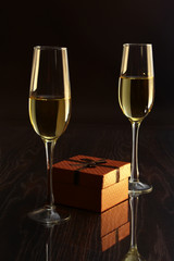 Two glasses with white wine and gift box on mirror table. Celebrities composition. Your text here.