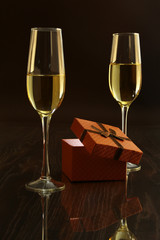 Two glasses with white wine and gift box on mirror table. Celebrities composition. Your text here.