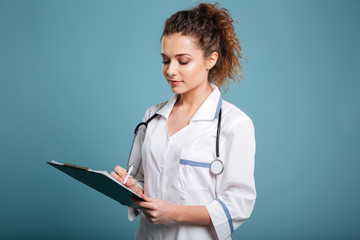 Young female doctor in uniform holding clipboard and writing