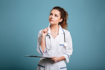 Thoughtful female doctor or nurse holding clipboard and looking up