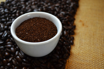 Ground coffee in white cup with coffee beans