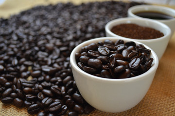 Coffee beans, ground coffee, and black coffee in white cups on burlap.