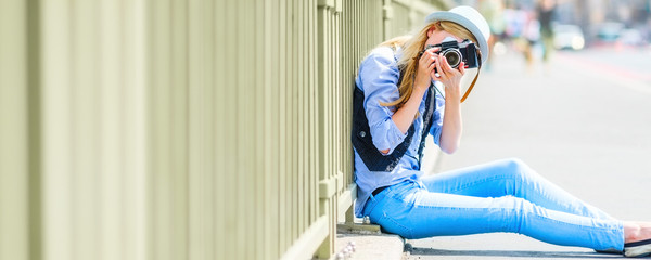 Hipster girl making photo with retro camera while sitting on city street © Alliance
