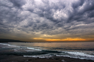Naklejka premium An ominously cloudy orange sunset over torrance beach in southern california as the waves roll in