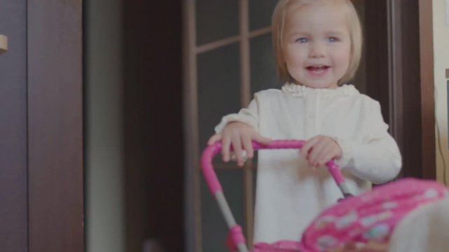 little girl plays a toy pram in the house