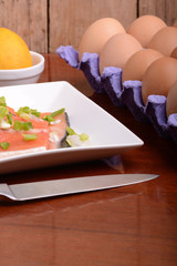 fresh salmon fillet close up on white plate. knife, eggs and lemon