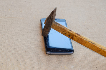Hammer and smartphone. The screen of the smartphone, a broken ha