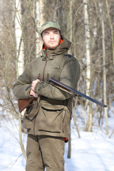 Fototapeta premium Hunter man with shotgun dressed in dark khaki clothing in the forest
