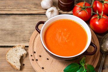 Tomato soup in ceramic bowl on wooden background.