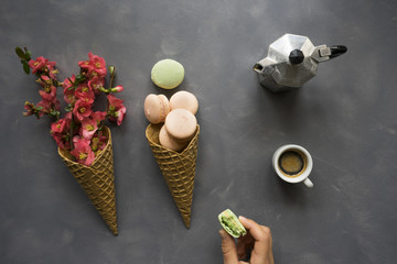 Coffee, macarons and flowers in ice cream cone on cement background