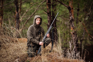 male hunter with binoculars ready to hunt, holding gun and walking in forest.
