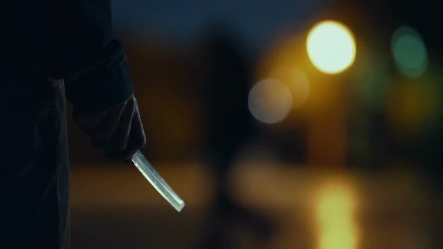 Killer with blade in hand shining at night stalking at park