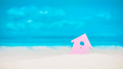 Symbol of little lilac house on the sand with bright cloudy blue painted sky background