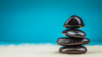 Growing piled up of four black pebbles on bright sand with blue background