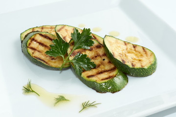 Grilled zucchini decorated with green leaf on white plate