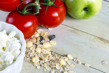 Foods for healthy eating: cottage chesse, tomatoes, apple, cereal on light wood background