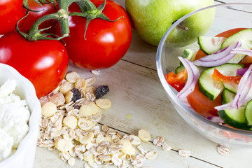 Foods for healthy eating: cottage chesse, tomatoes, apple, cereal on light wood background