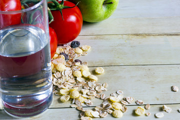 Foods for healthy eating: cottage chesse, pure water, tomatoes, apple, cereal on light wood background