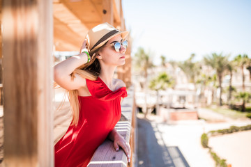 Young white girl standing on the pier in a red sun dress and hat.