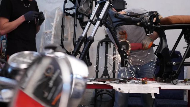 Young males mechanic assembling a custom cafe racer motorcycle in a garage