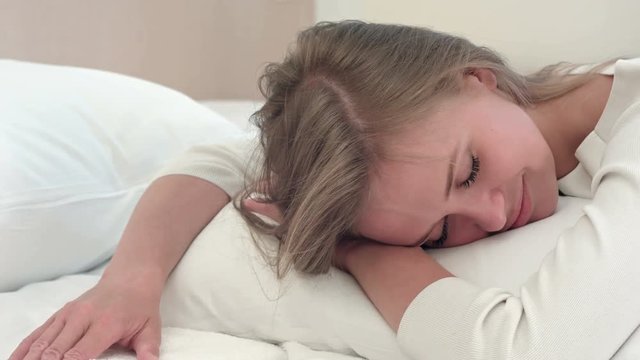 Relaxed young blonde girl sleeping on white bed at home or in hotel room