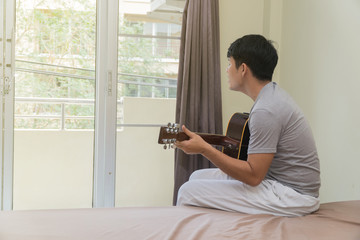 Behind the young man playing the guitar on bed in the bedroom.
