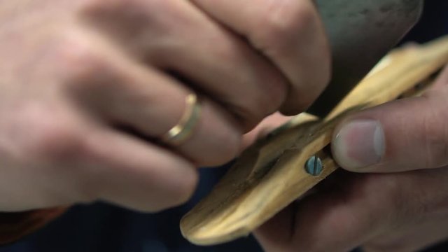 Man with an engagement ring on his hand processes with a help of a grinding paper the bridge of the guitar before painting