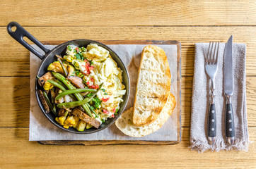 Omelet in a frying pan with vegetables, bread and cutlery