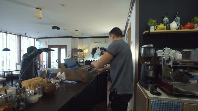Two African and Caucasian people walking into the shop and aiming to the assistant with guns. 4K gimbal stabilized shot