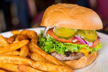 Burger with veggies, pickles, lettuce and french fries. 