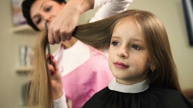 Close up view of professional hairdresser cutting long blond girls hair with scissors in beauty salon. Stylist doing hairstyle
