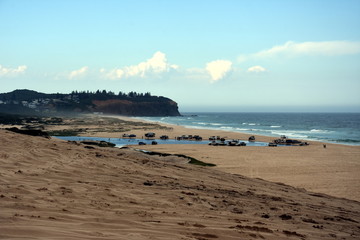 Horizontal landscape of the beach with cars. 4wd cars at Crokers creek (Belmont - Nine Miles - Beach, NSW, Australia). Redhead Point in the background.