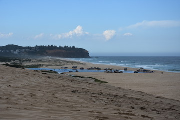 Horizontal landscape of the beach with cars. 4wd cars at Crokers creek (Belmont - Nine Miles - Beach, NSW, Australia). Redhead Point in the background.